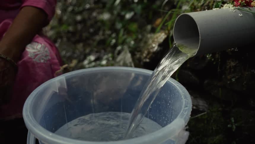 A person fetches water from a pipe into a bowl