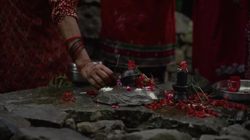 A close view of a religious ceremony where women in traditional clothing place red flowers and offerings onto stone artifacts