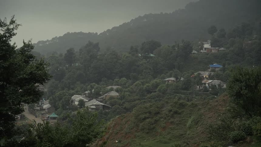 A rural village of simple houses sits on a misty green hillside under an overcast sky