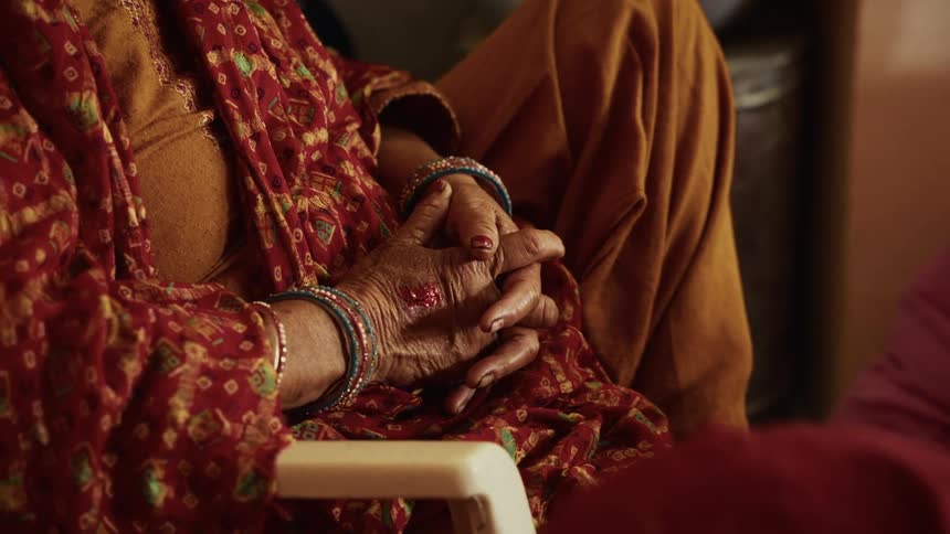 Elderly hands clasped together rest on patterned fabric in warm tones