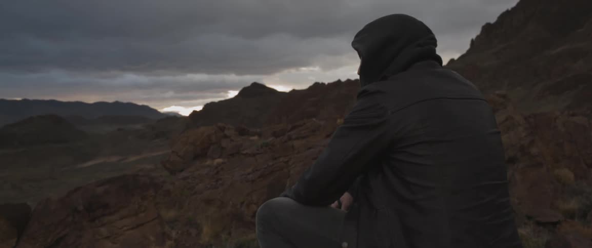 A man sits on the mountain with storm clouds in the distance