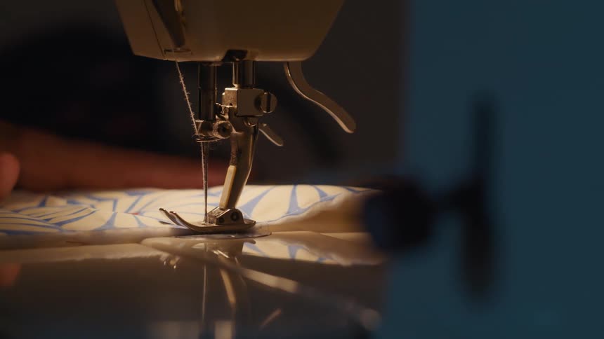 A close view shows a sewing machine needle moving up and down to sew fabric illuminated by a direct light source