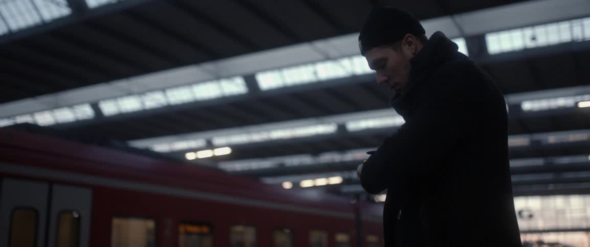 A man stands waiting in a subway station and looks at his watch
