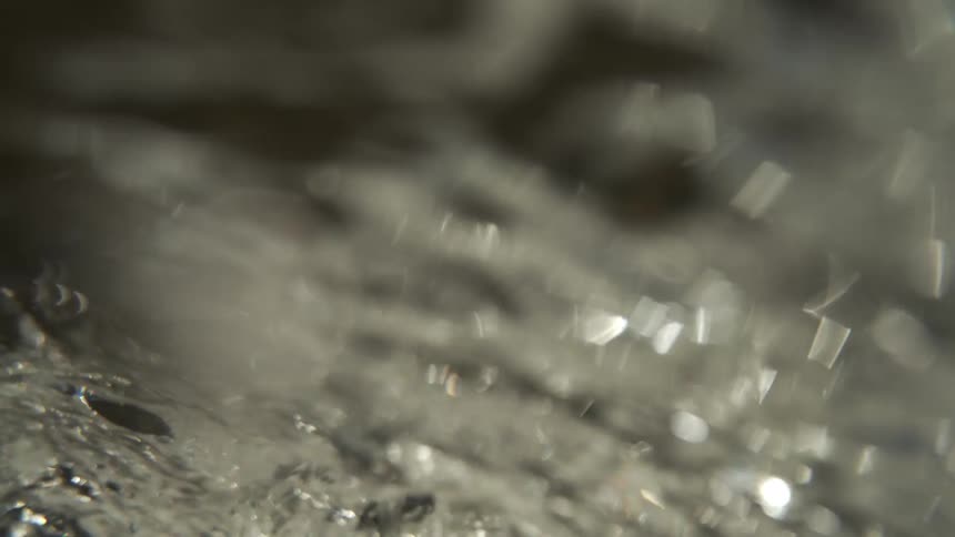 An extreme closeup view captures the rapid turbulent flow of clear water highlighting glistening bubbles and shifting textures in a handheld shot
