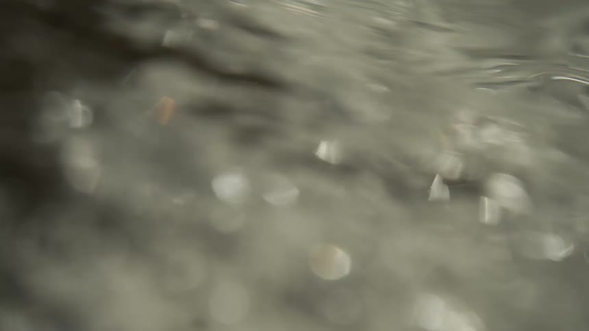 An extreme closeup of water features blurred shapes surface ripples and distinct circular bokeh reflections in the lower section