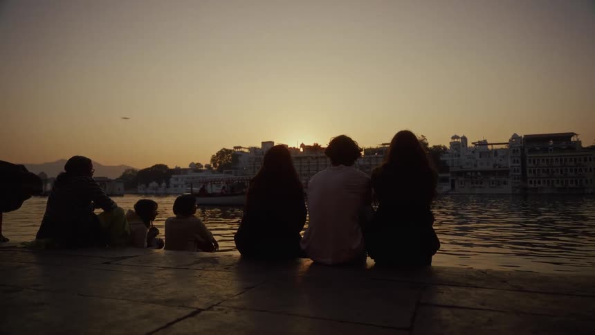 People are sitting by the shore line of the city at sunset
