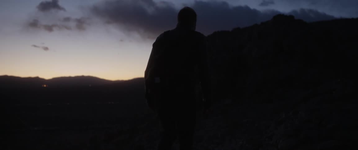 A man walking in a mountain area at sunset on a cloudy day