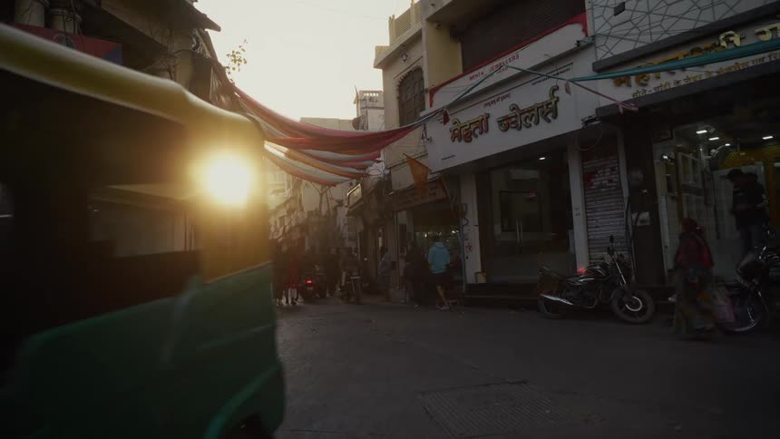 A busy street at sunset with people walking back and forth as motorcycles and tricycles drive past