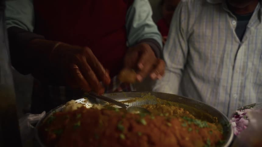 Hands serve hot food from a large dish in a busy setting