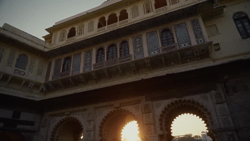 A low angle shot captures the ornate architecture of a historic palace or fort facade with arched entryways and detailed windows backlit by a setting sun