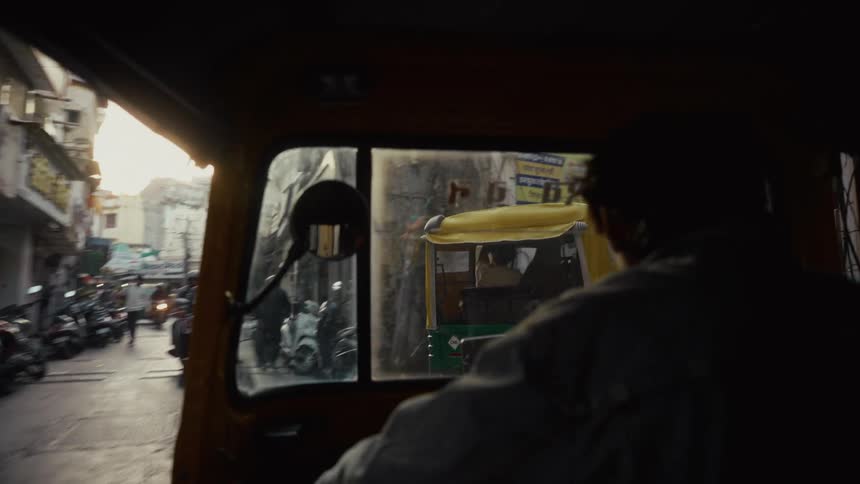 Busy street is seen from inside a small vehicle moving through a narrow alley