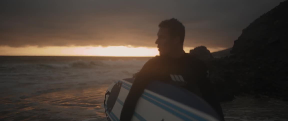 A man is walking near the water with a surfboard