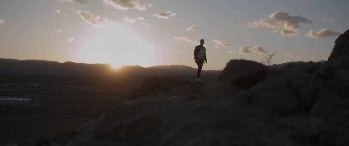 A man walking at the top of a mountain at sunset,