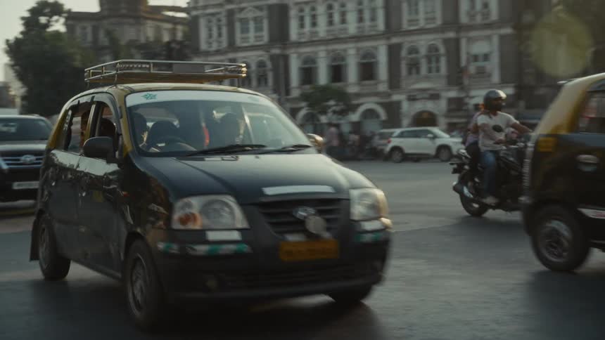 Black taxis driving along a busy avenue in an urban area with historic buildings in the background