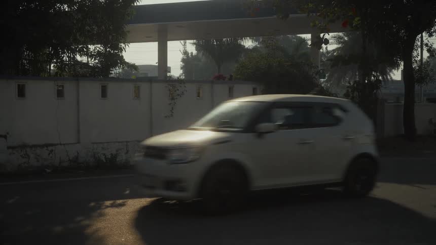 White car in motion turns on a shaded street beside a lightcolored wall
