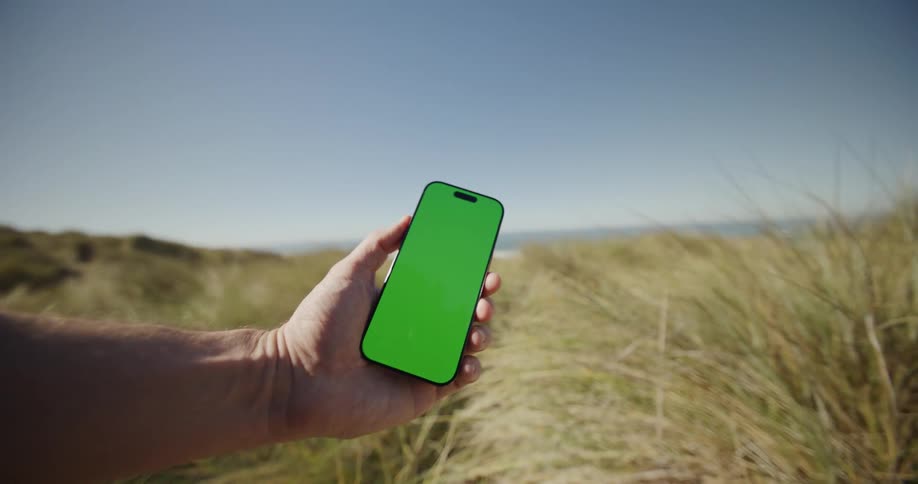 Hand holding a smartphone in the middle of a grassy area