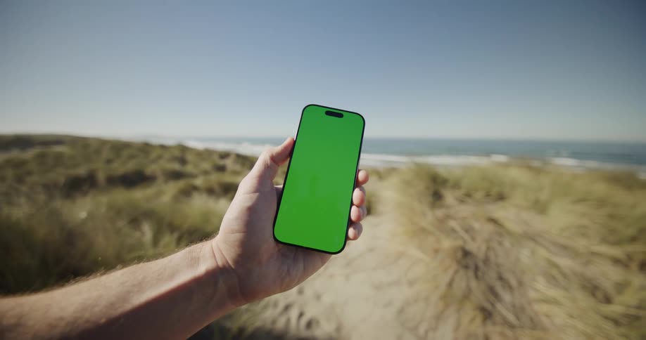 A man is holding his phone and turning at a beach
