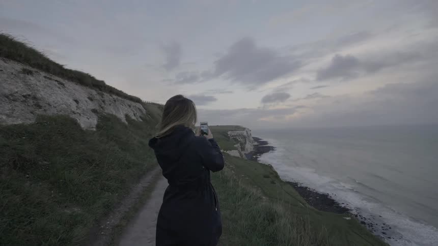 A woman is taking photographs of the shore with her phone