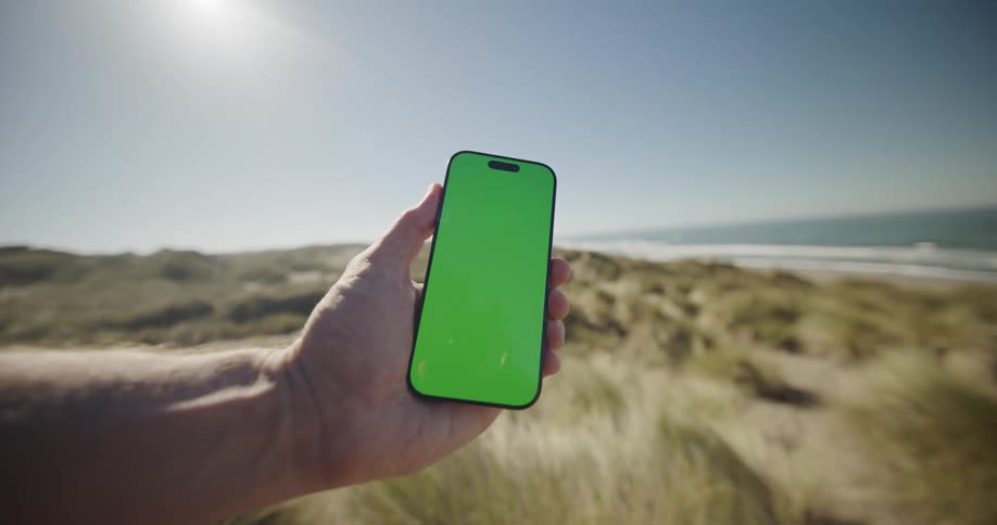 Hand holding a smartphone near the beach on a sunny day