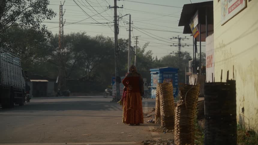 Two female adults with veiled heads talking in an alley next to an avenue with traffic on an underdeveloped urban area outdoors during day time