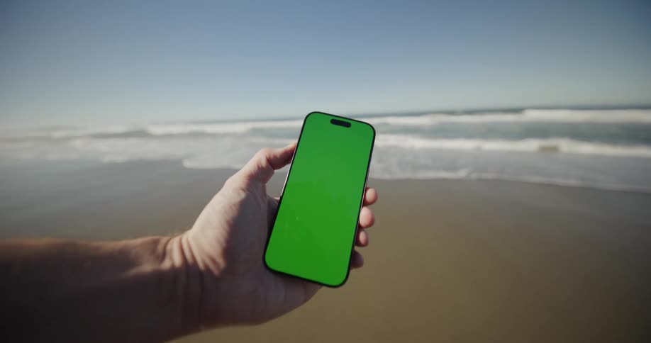A man holding a phone at the beach