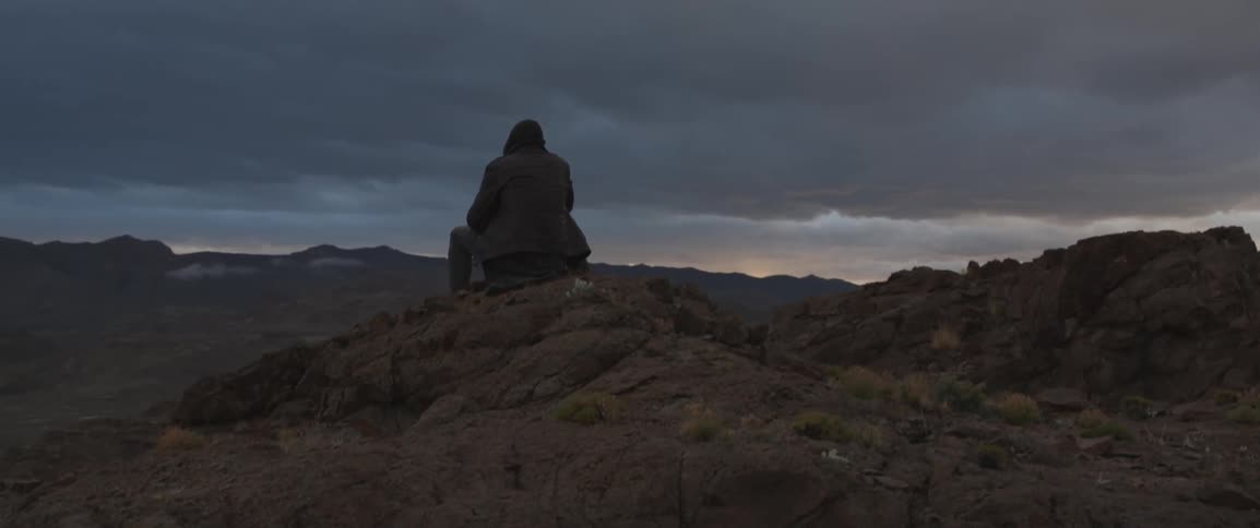 A man is sitting on rocks on a very cloudy day