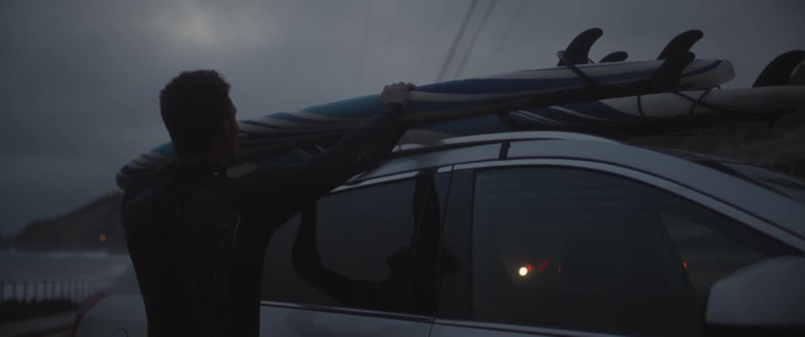 Man putting a surfboard on top of car