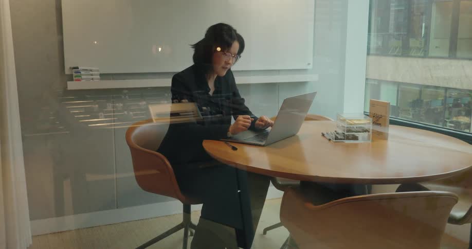 Woman works alone in meeting room with urban view through glass walls
