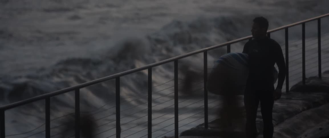 A surfer carrying his board walks on a boardwalk near the tide