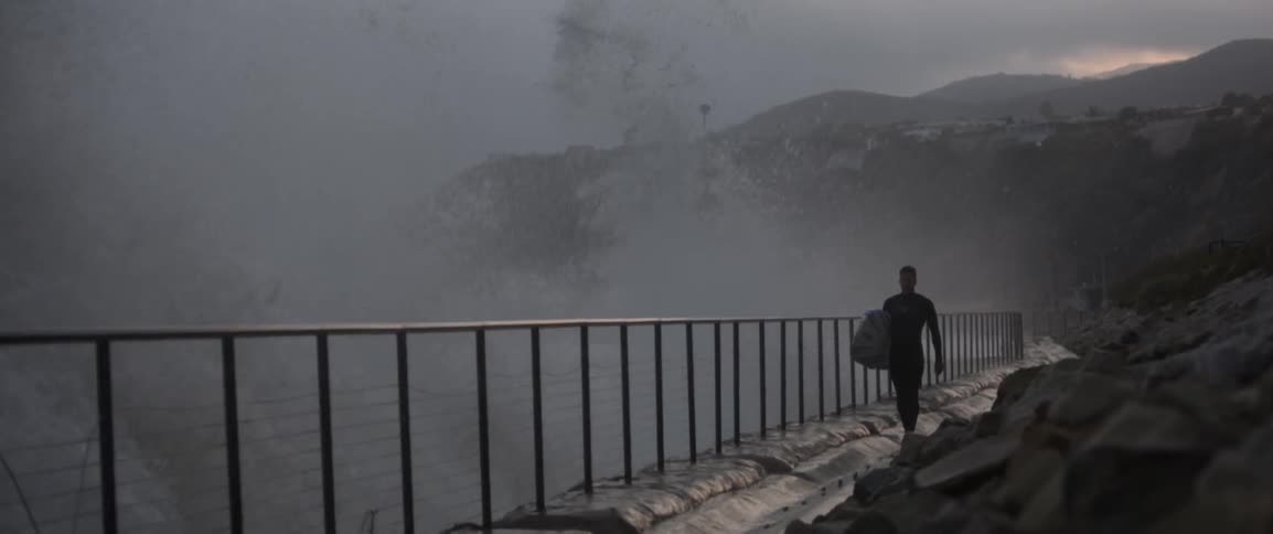 A man walks by a fence being hit by waves