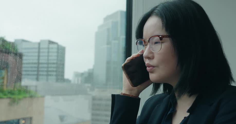 A woman stands next to an office building window while on her phone