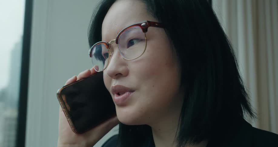 Woman holds her phone and talks as she stands near a window