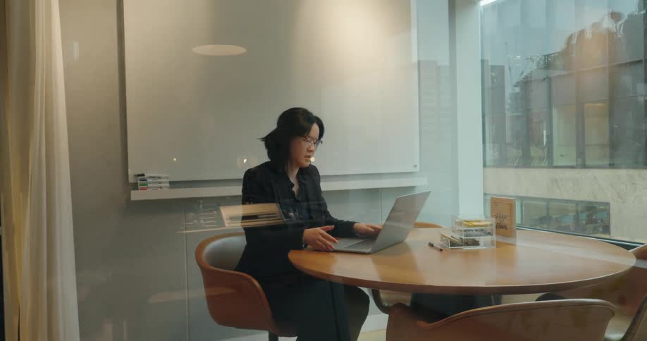 A professional businesswoman works on a laptop in a conference room