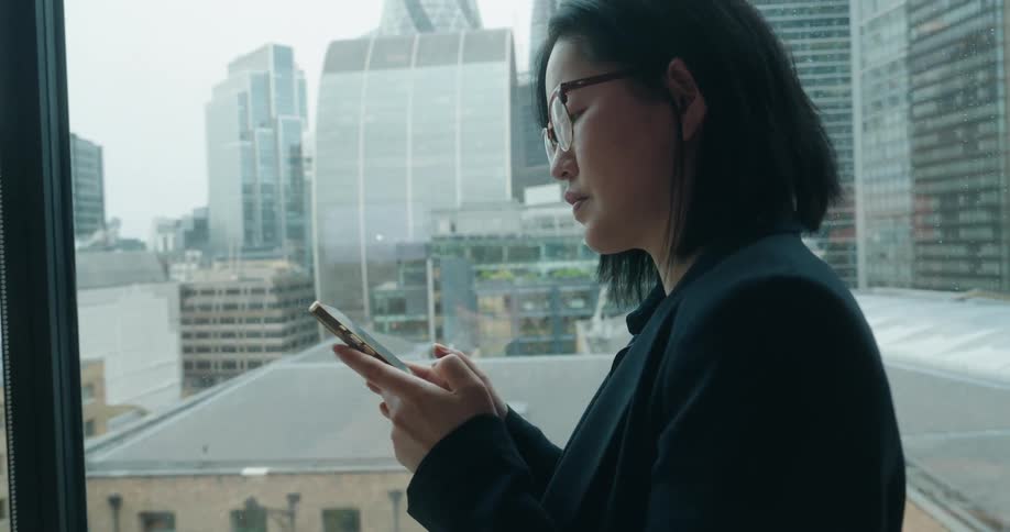 Woman holds her phone while looking at the screen with urban buildings in the background