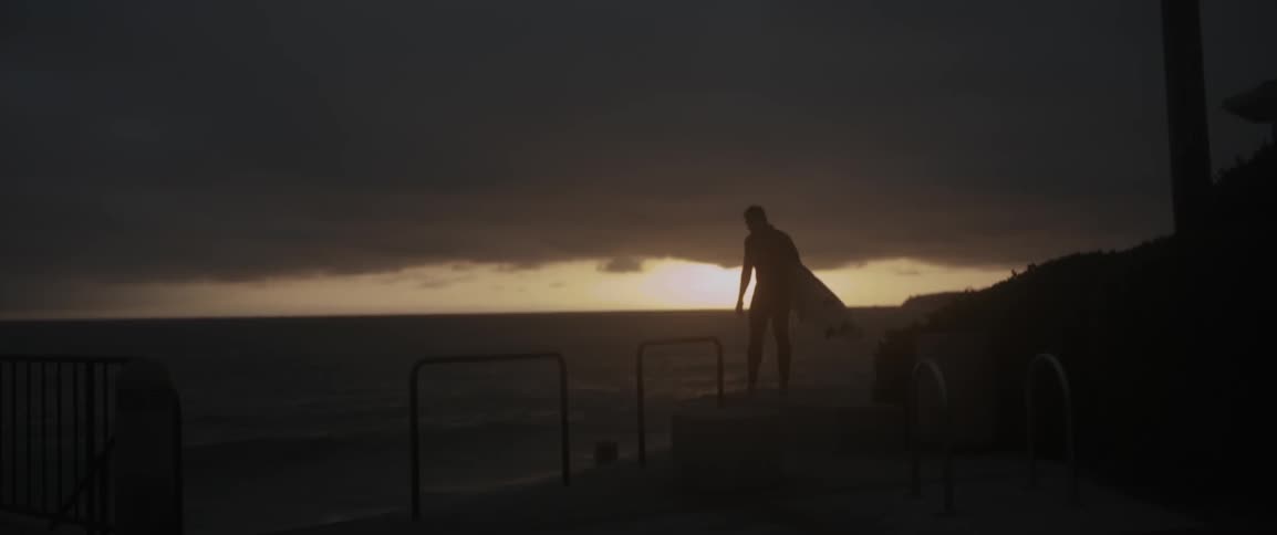 A man holding a surfboard at sunset turns around