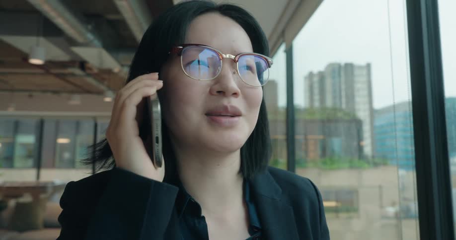 Young asian woman wearing formal black clothing talking on a phone indoors during day time
