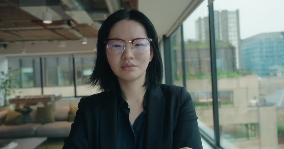 Woman wearing glasses with a serious demeanor in a glassenclosed corporate environment
