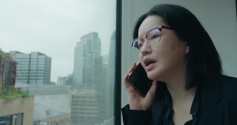 A woman talking on a phone in front of a window