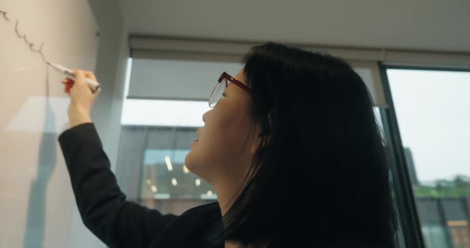 A woman in an office is using a marker to write on a whiteboard