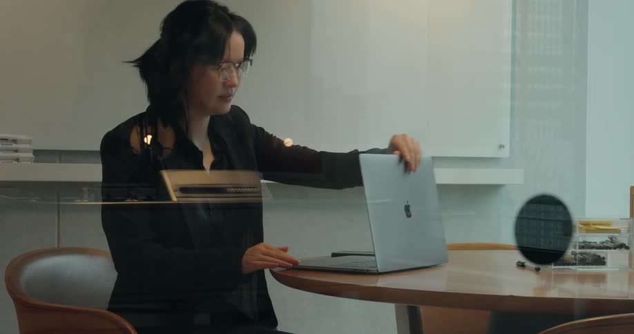 A professional woman sits at a desk working on her laptop in an office