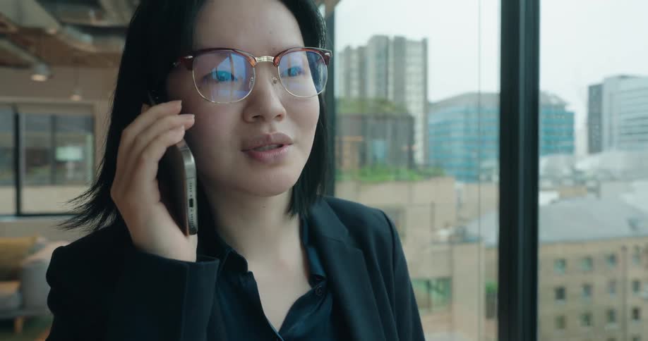 Woman talks on phone in modern office with urban view and foosball table in the background