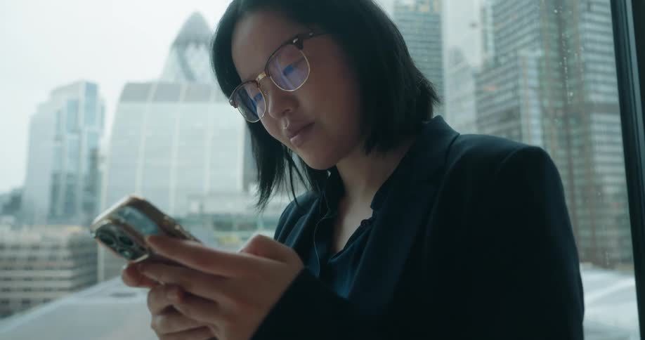 Woman looking at her phone in front of windows with corporate buildings in the background