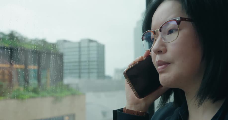 Woman holds her phone and talks as she stands near a window
