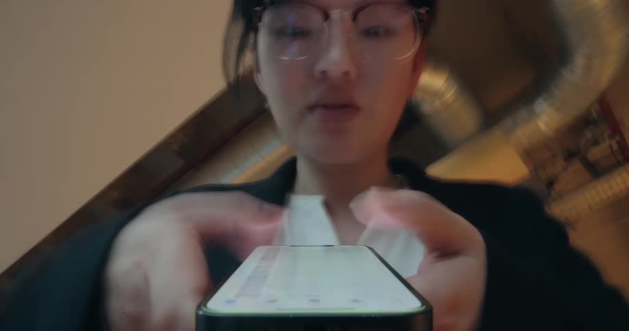 A young asian woman types on her smartphone while moving around the office at midday