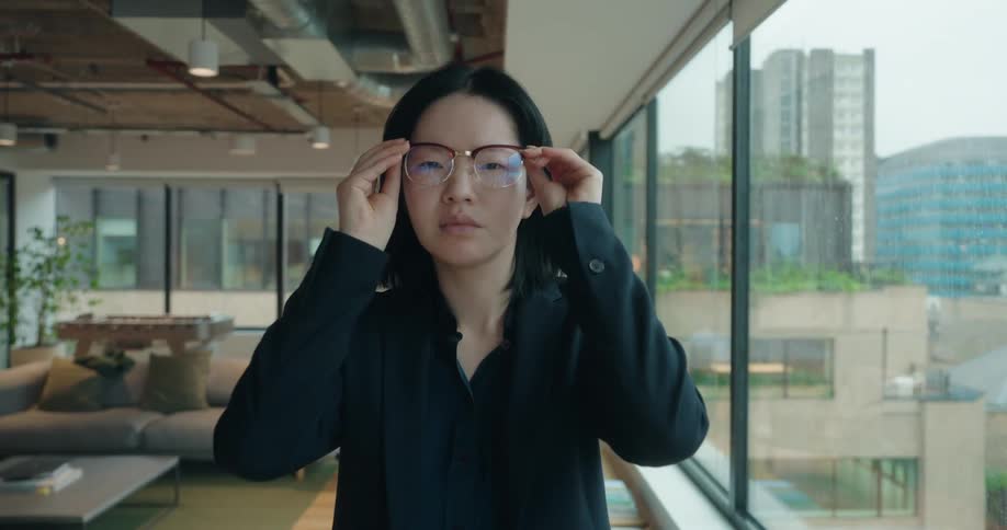 Professional in formal attire stands in a modern office with large windows