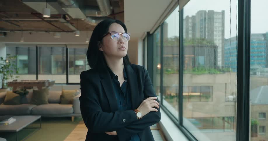 A woman wearing eyeglasses is looking out the high rise window