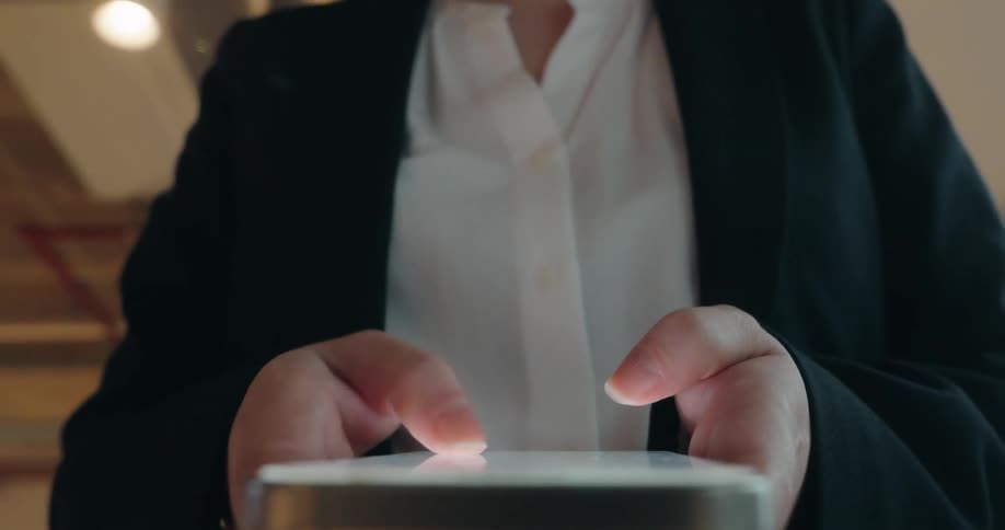 Person in dark blazer interacts with glowing mobile device screen beneath indoor structural lighting