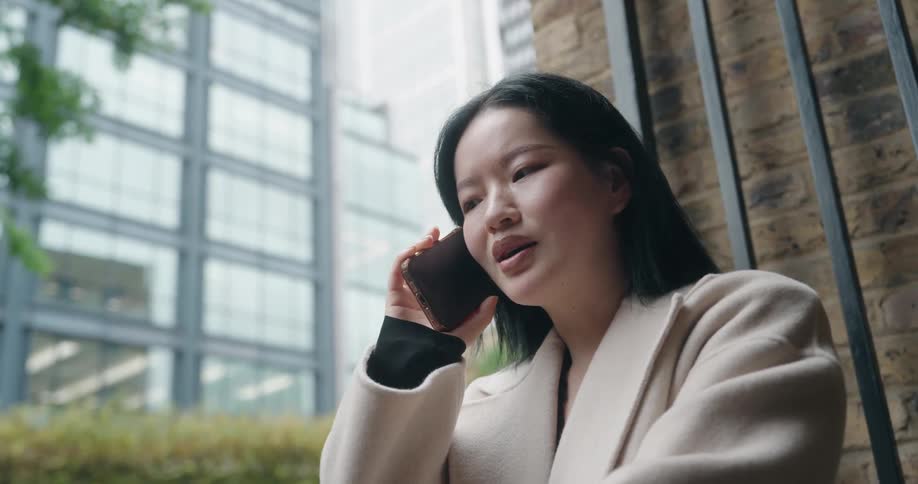 Woman standing outside next to a downtown building as she talks on her phone