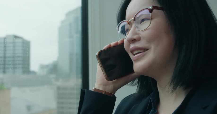 Woman talking on the phone while looking at the city through a building window