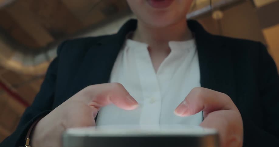 A woman in business attire types quickly on a smartphone with brightly glowing screen indicating a busy and focused task